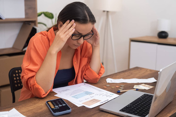 Stressz nő szemüvegben néz papír számlák érzés zavaros a magas fizetési arány hölgy problémái vannak, miközben összefoglalja közművek ül asztalnál az irodában - Fotó, kép