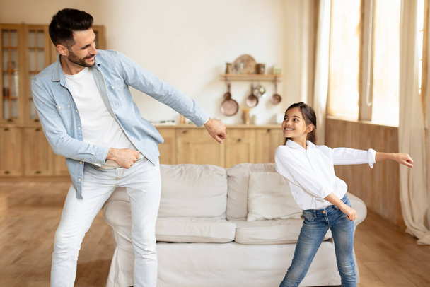 Lustige Freizeitbeschäftigungen. Fröhlicher hispanischer Vater und seine Tochter bewegen sich und tanzen zu Musik drinnen, haben Spaß beim Feiern, genießen die Zeit zu Hause in modernen Wohnzimmern - Foto, Bild