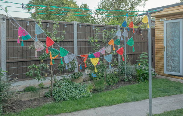 Bunting multicolor hecho de ganchillo adjunto a una línea de lavado en un jardín - Foto, imagen