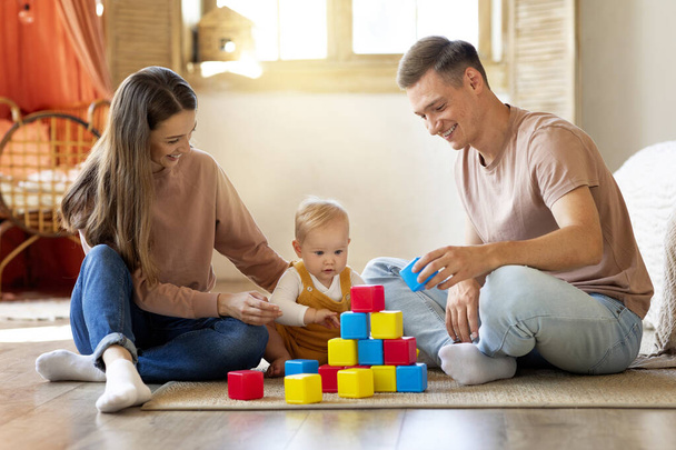 Щаслива молода кавказька сім'я грає разом зі своєю маленькою дитиною вдома, розважаючись з іграшковими будівельними блоками, люблячі батьки насолоджуються розвитком діяльності з немовлям - Фото, зображення