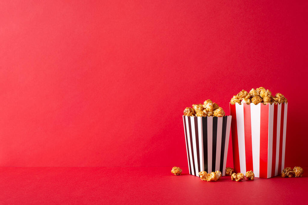 Cinematic rozkosz w najlepszym wydaniu: Stół z widokiem bocznym ułożone z serem i karmelowym popcornem w paski, pod czerwoną ścianą, gotowy do premiery filmu z przyjaciółmi - Zdjęcie, obraz