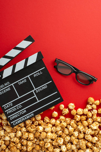 Függőleges felülnézet egy halom ízletes popcorn, 3D-s szemüveg, és egy film clapperboard élénk piros háttér, tökéletes film promóciók - Fotó, kép