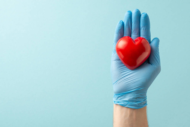 Podkreślić układ sercowo-naczyniowy z wysoką kompozycją kąta widzenia pokazującą dłonie w rękawiczkach medycznych obejmującą serce na miękkim niebieskim tle z przestrzenią do kopiowania tekstu lub reklamy - Zdjęcie, obraz