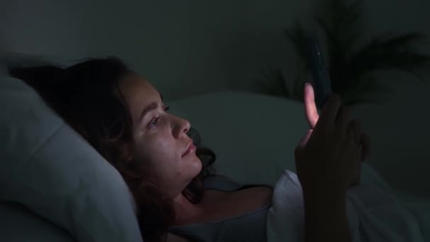 közelről éjszaka nő fekszik az ágyban, fogyasztja a telefonok képernyőjén, ábrázolása álmatlanság és okostelefon függőség küzd.  - Felvétel, videó