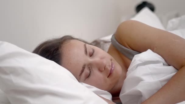 Beatitud del dormitorio: En un dormitorio sereno, una mujer joven duerme profundamente debajo de una manta blanca sobre su cómodo colchón ortopédico. - Imágenes, Vídeo
