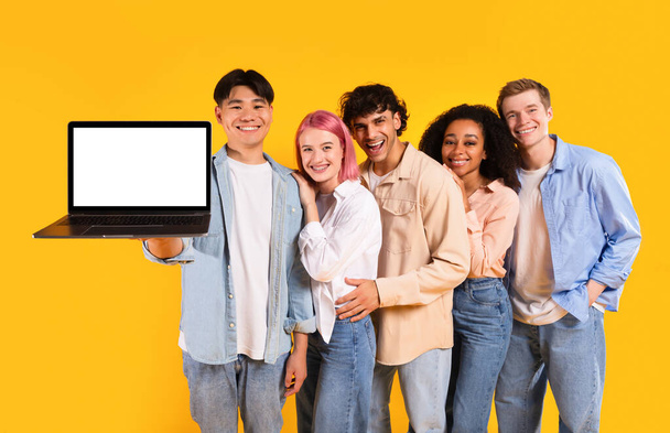 Cinque amici multirazziali che tengono il computer portatile che mostra lo schermo del computer vuoto, raccomandando il sito web educativo in piedi sopra lo sfondo giallo dello studio, mockup - Foto, immagini