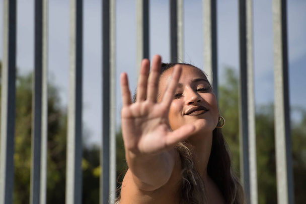 Latina und hispanisches Mädchen, jung und hübsch, bedeckt die Kamera mit ihrer Hand, während sie lächelt und scherzt. Konzeption Gesten, Witz, Spiel, hoch, ablehnen. - Foto, Bild