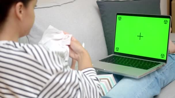 Consulta de Médico Virtual: Una mujer enferma, usando servilletas nasales, tiene una videollamada con su médico mientras está sentada en el sofá de la sala de estar en la comodidad de su hogar.  - Metraje, vídeo