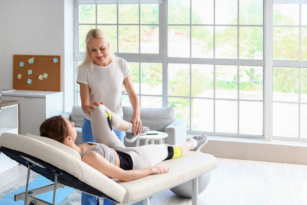 Fisioterapeuta femenina trabajando con una mujer joven en un sofá en un centro de rehabilitación - Foto, imagen