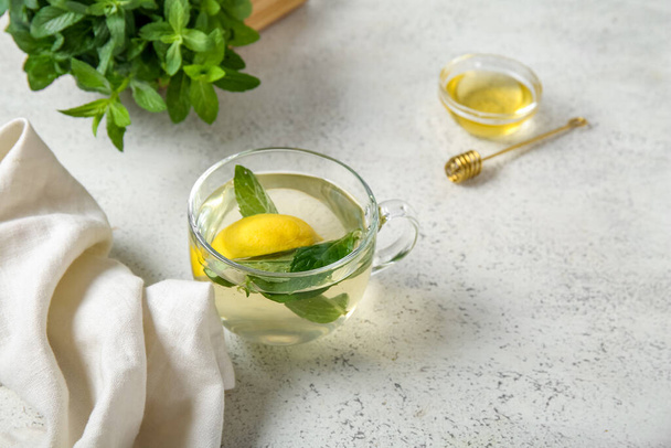 Чашка свежего мятного чая с лимоном и медом на большом светлом столе - Фото, изображение