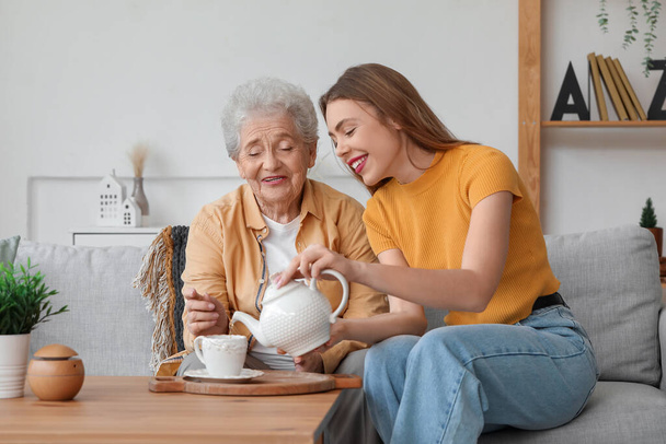 Genç bir kadın büyükannesi için fincana çay dolduruyor. - Fotoğraf, Görsel