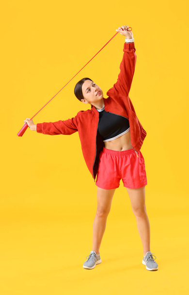 Sporty young woman training with jumping rope on yellow background - Photo, Image