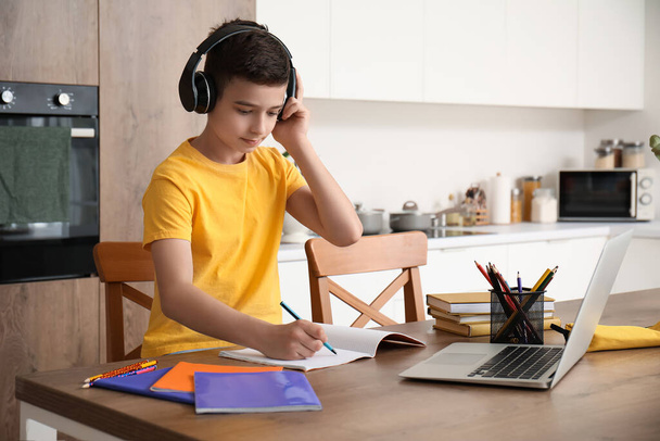Маленький хлопчик з навушниками та ноутбуком вивчає онлайн на кухні - Фото, зображення