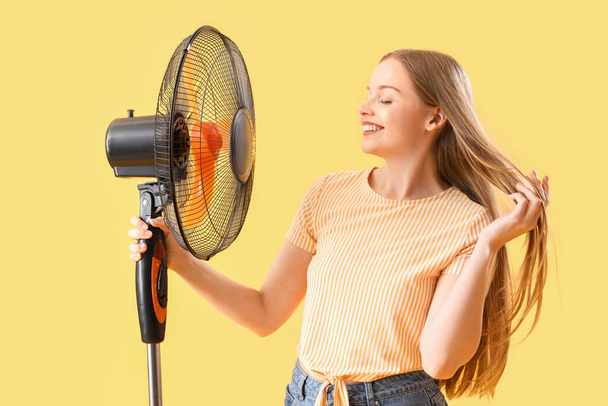 Jeune femme avec ventilateur électrique sur fond jaune - Photo, image