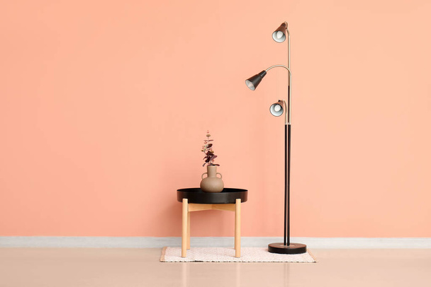 Standard lamp and vase with eucalyptus branches on small table near pink wall - Photo, Image
