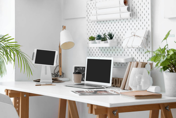 Posto di lavoro moderno con dispositivi, pegboard e piante d'appartamento in ufficio leggero - Foto, immagini