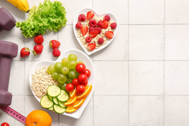 Тарелки со свежими здоровыми продуктами, измерительная лента и гантели на светлом фоне плитки. Концепция питания - Фото, изображение
