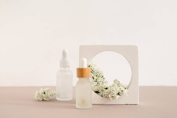 Skład z butelkami olejku eterycznego, podium gipsowego i pięknymi kwiatami na jasnym tle - Zdjęcie, obraz