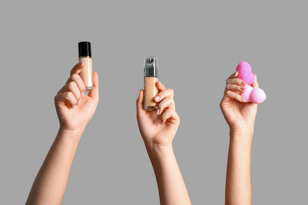 Manos femeninas con esponjas de maquillaje y botellas de base sobre fondo gris - Foto, Imagen