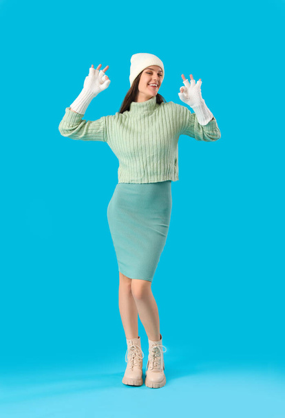 Νεαρή γυναίκα με χειμωνιάτικα ρούχα σε μπλε φόντο - Φωτογραφία, εικόνα