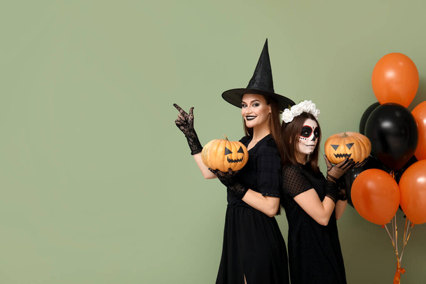 Giovani donne vestite per Halloween con zucche e palloncini su sfondo verde - Foto, immagini