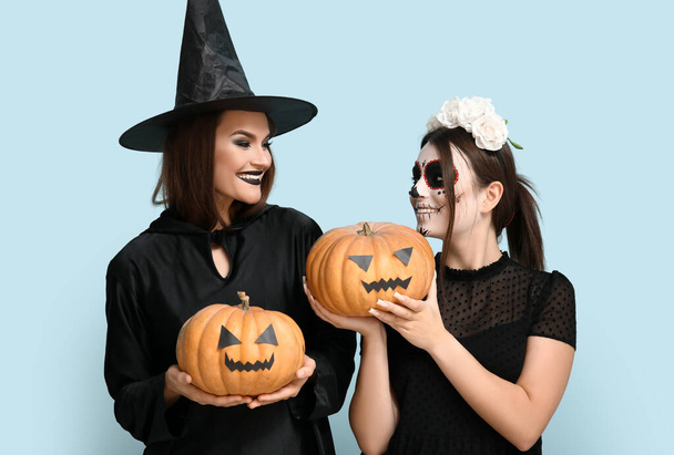 Jovens mulheres vestidas para o Halloween com abóboras no fundo azul - Foto, Imagem