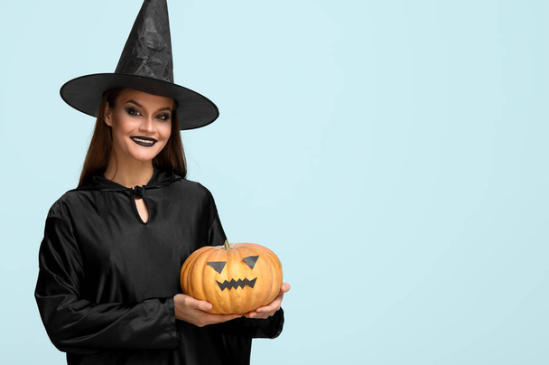 Młoda kobieta ubrana na Halloween jako czarownica z dynią na niebieskim tle - Zdjęcie, obraz