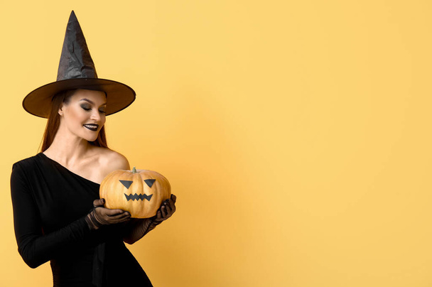 Junge Frau verkleidet sich zu Halloween als Hexe mit Kürbis auf gelbem Hintergrund - Foto, Bild