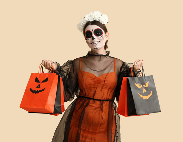 Jeune femme habillée pour Halloween avec des sacs-cadeaux sur fond beige - Photo, image