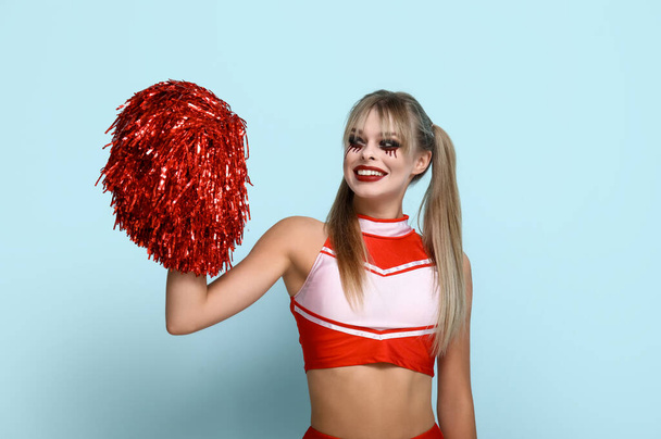Jonge vrouw gekleed voor Halloween als cheerleader op blauwe achtergrond - Foto, afbeelding
