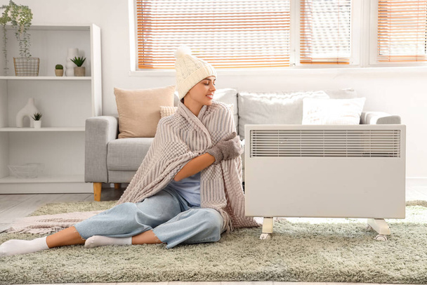 Mujer joven con calentamiento a cuadros cerca del radiador en casa - Foto, imagen