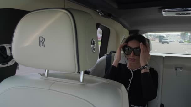 Dubai, BAE - 114 2023: zarif siyah elbiseli esmer kadın ve pahalı şık bir limuzinin kabininde güneş gözlüğü. Yaklaş, Ağır çekim.. - Video, Çekim