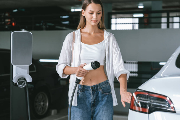 Fiatal nő utazás EV elektromos autó bevásárló központ parkoló töltés a belvárosban mutatja városi fenntarthatóság életmód zöld tiszta újratölthető energia elektromos jármű belsejében - Fotó, kép