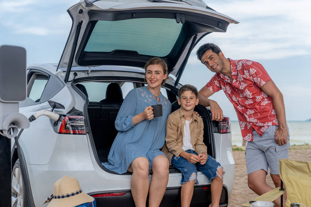 Семейный отдых на пляже с электромобилем, счастливая семейная поездка на автомобиле Harge EV, наслаждаясь кофе на свежем воздухе. Морской транспорт и экологически чистый автомобиль для чистой окружающей среды. Вечный - Фото, изображение