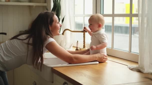 Happy family at home. Mother playing with little toddler child in kitchen. Mom baby relax playing having fun together. Mother looks at baby with love care. Mom of breast feeding baby rest at home - Footage, Video