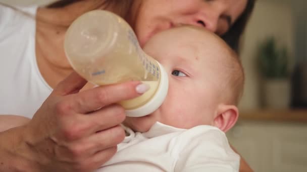Счастливая семья дома. Мать держит маленького малыша ребенка, кормящего молоко из бутылки. Новорожденная малышка сосёт питьевое молоко. Мама кормящего грудью ребенка. Материнство счастливый ребенок - Кадры, видео