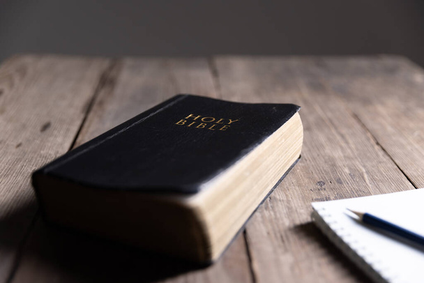 Heilige Bijbel op de houten tafel. Heilige bijbel met notitieboek en potlood op houten tafel tegen ochtendzonlicht voor christelijke devotie, kopieer ruimte - Foto, afbeelding