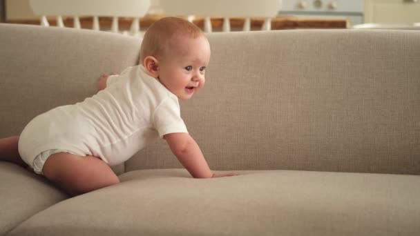 Boldog baba. Aranyos kis újszülött lány mosolygó arccal mászkál a kanapén a hálószobában. A csecsemőbaba otthon pihen a kanapén. Az anyaság boldog gyermekgondozási koncepciója - Felvétel, videó
