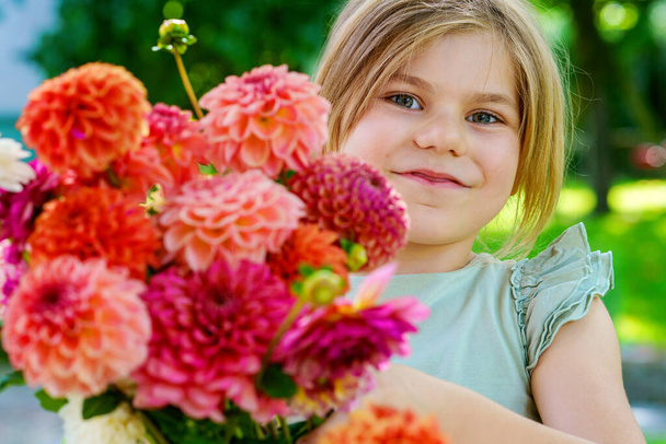 Nahaufnahme eines kleinen Vorschulmädchens mit Dahlienblütenstrauß. Nahaufnahme eines glücklichen Kindes, das bunte Sommerblumen für den Muttertag oder Geburtstag in den Händen hält. Nahaufnahme von Blumen in Regenbogenfarben - Foto, Bild