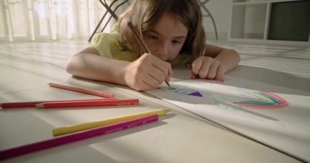 Un bambino carnivoro disegna con una matita su carta sul pavimento di casa. Una ragazza creativa è impegnata nell'arte. Filmati 4k di alta qualità - Filmati, video