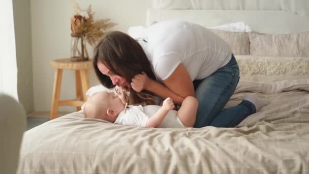Ευτυχισμένη οικογένεια στο σπίτι. Η μητέρα παίζει με ένα μικρό παιδί στο κρεβάτι. Μαμά μωρό χαλαρώστε παίζοντας διασκεδάζοντας μαζί. Η μητέρα κοιτάζει το μωρό με αγάπη. Μαμά του θηλασμού μωρό ανάπαυση στο σαλόνι - Πλάνα, βίντεο