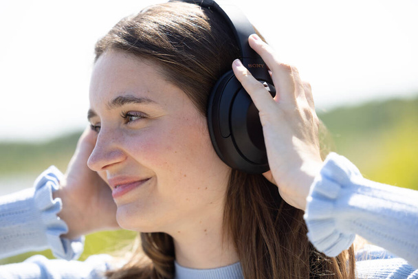 Experience the captivating sight of a pretty and attractive young millennial woman immersed in her world of music, courtesy of wireless headphones. Her serene face reflects the pure joy of nature and - Photo, Image