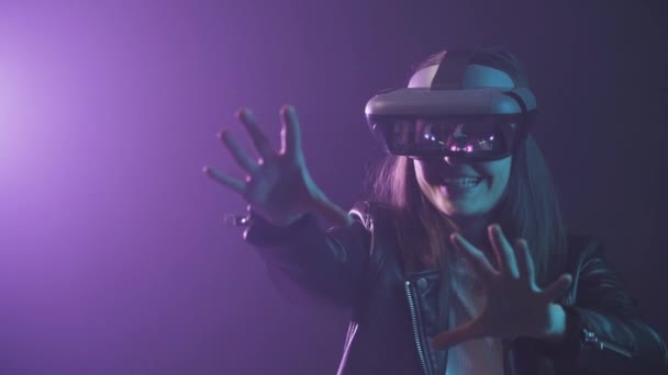Unerkennbare Frau mit ausgestrecktem Arm trägt VR-Headset beim Erkunden der virtuellen Realität unter blauem Neonlicht in Wandnähe mit Projektor-Beleuchtung - Filmmaterial, Video