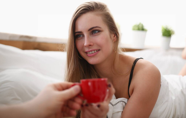 young pretty blond woman have cup of tea coffee early morning in her bed - Photo, Image