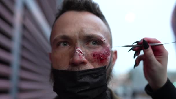 Макіяж художник змащує фарбу людиною з бородою і маскою для обличчя  - Кадри, відео