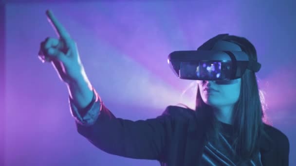 VRヘッドセットを着用しながら、プロジェクター照明付きの壁の近くの青ネオンライトの下で仮想現実を探索し、外側の腕を持つ認識できない女性の側面図 - 映像、動画