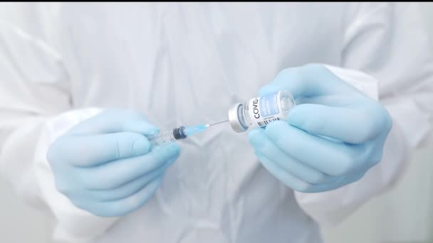 Gewasgerichte professionele mannelijke arts in chirurg toga handschoenen en gezichtsscherm vullen spuit met medicatie van de injectieflacon tijdens het werken in een modern uitgerust ziekenhuis - Video