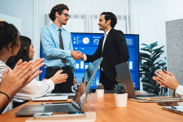 Two businessman shake hand in meeting room with coworker give cheerful applause. Team of analyst celebrate after successful significant progress on business strategic performance. Habiliment - Photo, Image