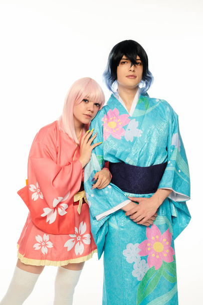 blond anime stijl vrouw leunen op extravagante man in kleurrijke kimono op wit, cosplay personages - Foto, afbeelding