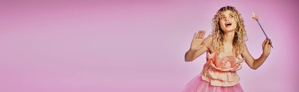 kaunis kihara tukka nainen nosti kädet ja taikasauva poseeraa vaaleanpunainen tausta, banneri - Valokuva, kuva